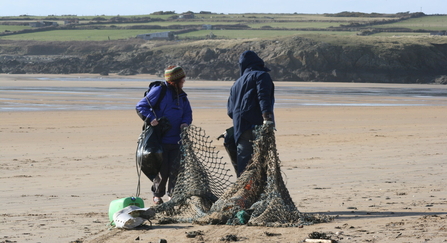 Two people pulling litter from a beach